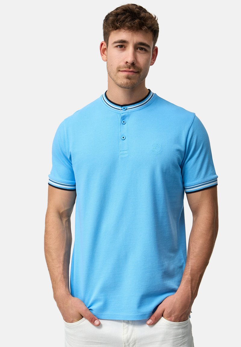 Polo de culoare bleu deschis cu guler tip henley, detalii contrastante în dungi negre și albe pe guler și mâneci, având trei butoane.
