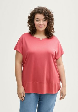 Haut corail ample à manches courtes, décolleté en V et ourlet texturé, associé à un pantalon en denim bleu clair.