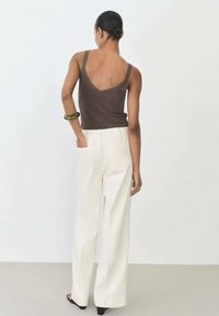 Brown knitted tank top with a v-back, paired with high-waisted, wide-leg white trousers and a green bracelet on the left wrist.
