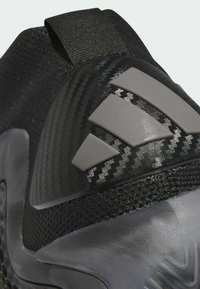 Közelkép fekete sportcipő sarkáról, amely texturált anyagból készült, karbon mintával és három szürke gumisávval rendelkezik, átlátszó talpon.