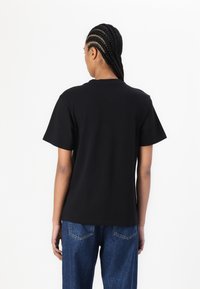 Black cotton T-shirt with short sleeves and a crew neck, featuring a relaxed fit and smooth texture. Paired with blue denim jeans.