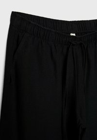 Pantalon noir à coupe ample avec taille élastique et cordon, doté de poches latérales et d'une texture de tissu lisse.