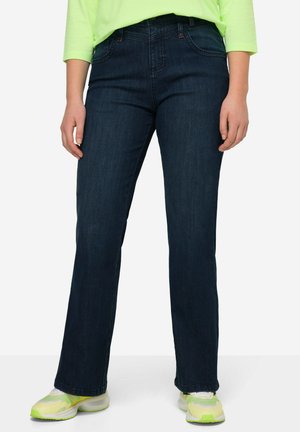 Jean en denim bleu foncé avec une coupe droite, comportant des poches avant et un design classique à cinq poches. Porté avec des chaussures vert néon.