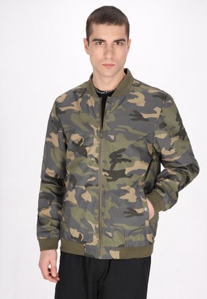 Camo bomberjakke i grønne, beige og grå nuancer; har en frontlynlås, ribbet krave og lommer på begge sider. Glat tekstur.