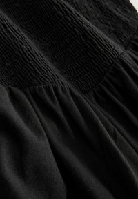 Robe noire avec un haut texturé présentant des motifs en relief et une partie inférieure froncée, fabriquée dans un tissu doux à la texture lisse.