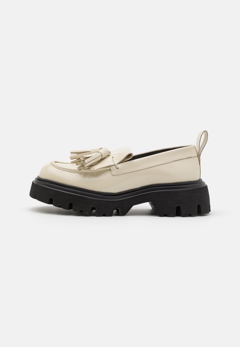Mocassin en cuir couleur crème avec semelle noire crantée épaisse et décoration à pampilles, doté d'une languette arrière pour un enfilage facile.