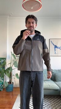 Vodonepropusna jakna tamnosive i crne boje s zatvaračem, kapuljačom i bočnim džepovima. Nosena je uz tamne traperice u dnevnoj sobi.