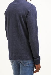 Long-sleeve navy blue shirt with a textured pattern, round neck, and ribbed cuffs, paired with light blue jeans.