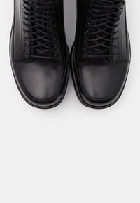 Zapatos altos de cuero negro con un acabado suave, que cuentan con una puntera redonda y múltiples ojales con cordones para un ajuste seguro.