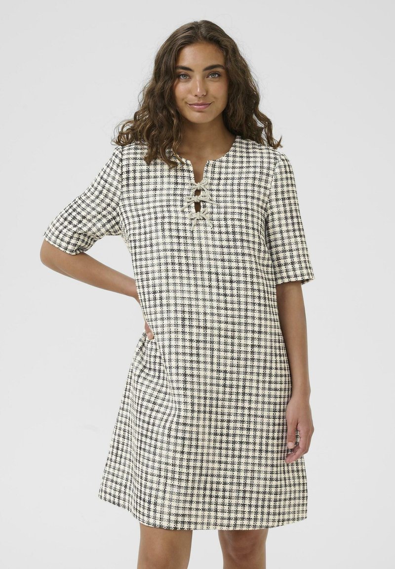 Kratka haljina s kratkim rukavima i kariranim uzorkom u crnoj i krem boji. Ima dekolte u obliku ključanice i slobodan kroj, izrađena je od teksturiranog materijala.