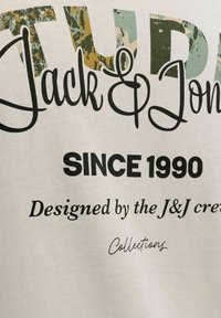 Biała bawełniana koszulka z nadrukiem tekstowym. Zadruk w odważnej czarnej i kamuflażowej czcionce z napisami "Jack & Jones" oraz "Since 1990".