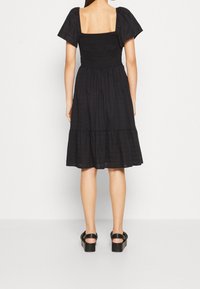 Schwarzes Kleid mit quadratischem Ausschnitt, Puffärmel, gerafftem Oberteil und gestuftem Rock. Getragen mit schwarzen Plateausandalen.