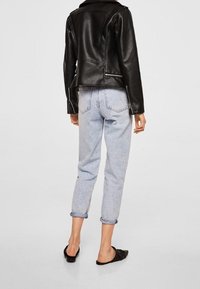 Giacca di pelle nera con una silhouette leggermente aderente, abbinata a jeans azzurri con risvolto e scarpe nere basse. Texture complessivamente liscia.