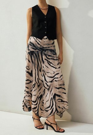 Femme portant un gilet noir sans manches boutonné, une jupe beige et noire à imprimé tigre, des sandales à talons noires à lanières et un collier en argent.