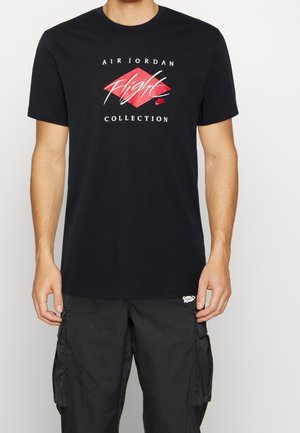 Mand iført sort Air Jordan Flight Collection t-shirt og sorte cargobukser mod en ensfarvet hvid baggrund.