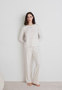 Haut à manches longues blanc et pantalon assorti, fabriqués en tissu doux. Présente une légère extensibilité avec un col rond et un branding minimal.