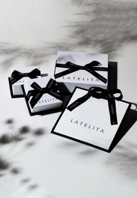 Tre scatole regalo bianche con nastro nero, con la scritta "LATELITA". Di diverse dimensioni, con semplici accenti neri e superfici lisce.