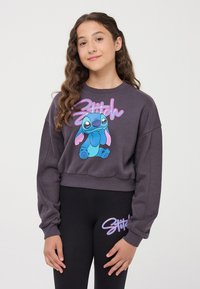 Szary, krótki sweatshirt z grafiką Sticha w kolorze niebieskim, z różowymi akcentami. Czarne legginsy z napisem "Stitch" w dopasowanym różowym kolorze.