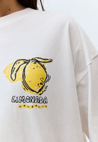 Sweat-shirt crème surdimensionné avec un motif de citron jaune aux contours noirs, et le texte "LIMONADA VALENCIA" en dessous. Matière coton douce.