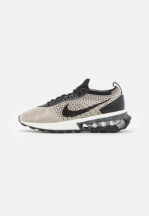 Beżowo-czarny sneaker Nike z dzianinową cholewką, czarnym logo Swoosh, podeszwą z amortyzacją powietrzną oraz czarną gumową podeszwą zewnętrzną, widok z boku.