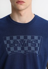 Tmavě modré bavlněné tričko s motivem šachovnice a světle šedým logem "Levi's" uprostřed hruď. Krátké rukávy, kulatý výstřih.