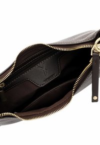 Interno di una borsa in pelle marrone con zip dorata, foderato in tessuto scuro, una tasca con zip e una toppa in pelle con marchio. Texture liscia in tutto.