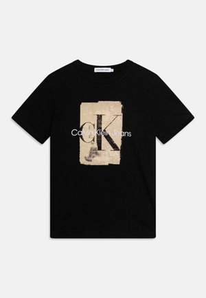 Camiseta de algodón negra con un gráfico rectangular en dorado y beige que presenta una "K" grande y el texto "Calvin Klein Jeans" en blanco. Mangas cortas.