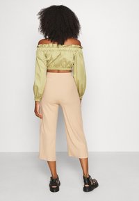 Haut court vert olive, décolleté épaule dénudée avec des poignets élastiques, associé à un pantalon large beige côtelé, complété par des chaussures noires à lanières.