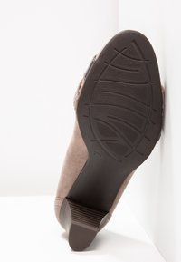 Chaussure en daim marron avec une semelle en caoutchouc noir texturée et un talon bloc, présentée semelle vers le haut sur un fond blanc.
