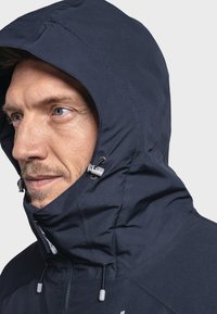 Marineblauwe hoodie met een gestructureerd oppervlak, verstelbare trekkoorden en een aansluitende kraag. Voorzien van grijze hardware bij de nek en kin.