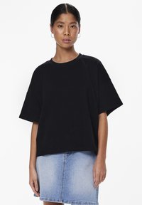 Svart oversized t-shirt med korta ärmar och rundad halsringning, ihopparad med en ljus jeanskjol. Tyget ser slätt och mjukt ut.