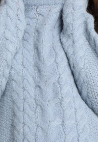 Himmelblaues Strickpullover mit strukturierten Zopfmustern, weichem Erscheinungsbild und einem gemütlichen, dicken Stoff.