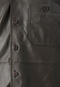 Dunkelbraunes Lederhemd mit durchgehender Knopfleiste, kleiner Brusttasche und sichtbaren Nähdetails. Weiche Textur mit matter Oberfläche.