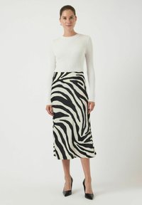 Vit ribbad långärmad topp i kombination med en midikjol i svart och vit zebra-mönster, bärs med svarta högklackade skor. Slät tygtextur.