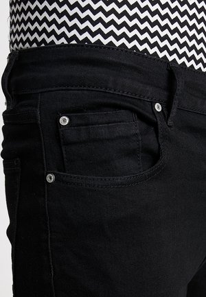 Nahaufnahme einer schwarzen Denim-Jeanstasche mit silbernen Nieten, getragen mit einem schwarz-weiß gemusterten Oberteil mit Zickzackmuster.