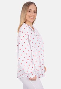 White button-up shirt made of crinkled fabric with red heart patterns. Features a collar and long sleeves. Button closure.