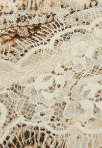 Gros plan sur un tissu en dentelle crémeux avec des motifs floraux superposés sur un textile texturé brun et beige à motifs.