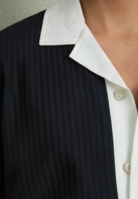 Cămașă cu dungi marine, dotată cu un guler alb clasic și închidere cu nasturi. Țesătura are un aspect texturat, cu dungi verticale.