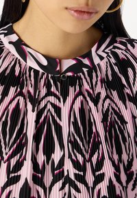 Faltenkleid mit hohem Kragen, überwiegend pink mit schwarzen und fuchsia-farbenen abstrakten Mustern, abgeschlossen mit einem kleinen metallischen Knopf.