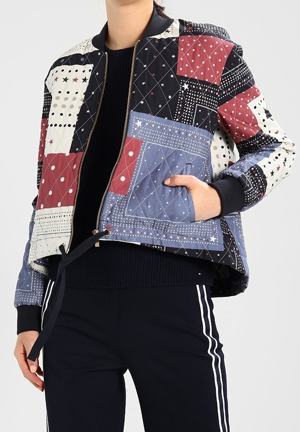 Veste bomber matelassée avec un mélange de patchs géométriques en rouge, bleu, noir et crème. Dotée d'une fermeture éclair et de poignets contrastants.