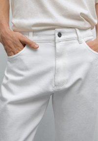 Pantaloni in denim bianco a vestibilità slim, con tasche frontali, chiusura con bottone e dettagli di cucitura discreti sul tessuto.