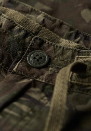 Détail de tissu camouflage avec un bouton sombre gravé "Superdry", couture piquée, ceinture texturée et cordon de serrage.