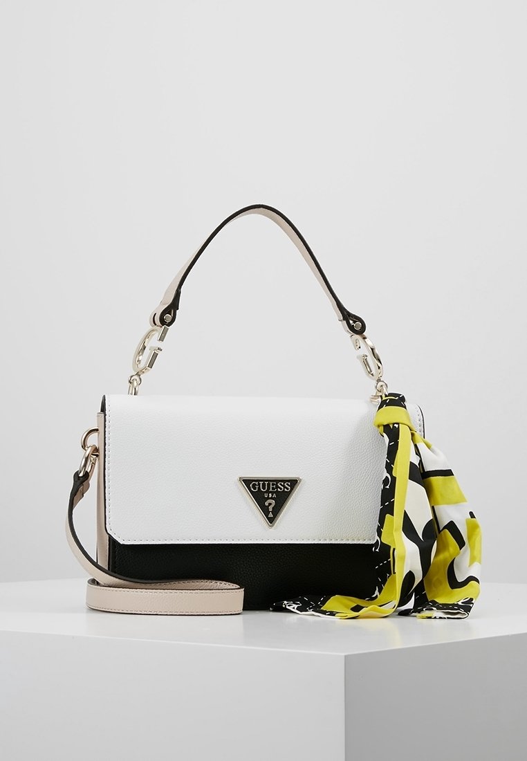 Borsa Guess bianca e nera con tracolla beige e foulard giallo-nero annodato al manico, esposta su una superficie bianca.