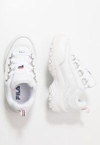 Baskets de sport blanches avec une tige en cuir synthétique, un col rembourré, un design à lacets, une semelle texturée et un accent rouge et bleu au niveau du talon.