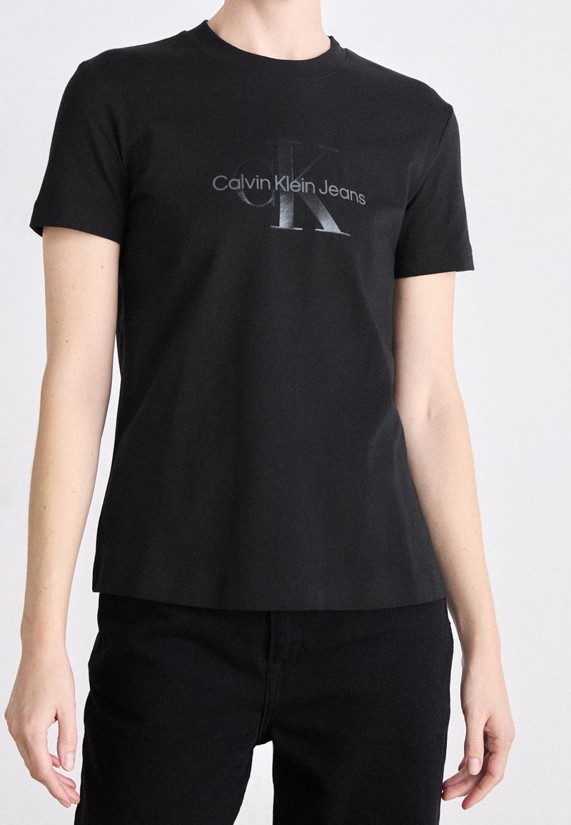 Czarny t-shirt z krótkim rękawem wykonany z bawełny, z odblaskowym srebrnym logo "Calvin Klein Jeans" na przodzie.