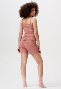 Jasnoróżowy top na ramiączkach i pasujące szorty, wykonane z miękkiego materiału. Szorty mają luźny krój, a całość dopełniają prążkowane skarpetki w pastelowych kolorach.