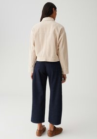 Beige Cordjacke mit Kragen, verkürzt geschnitten, kombiniert mit dunkelblauen weit geschnittenen Jeans und braunen Sneakern, von hinten betrachtet.