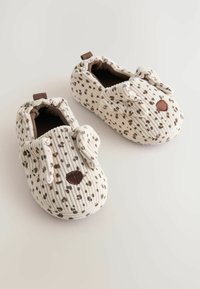 Chaussons pour bébé doux avec un motif tacheté beige et marron, conçus avec des oreilles de chien tombantes et un nez marron à l'avant.