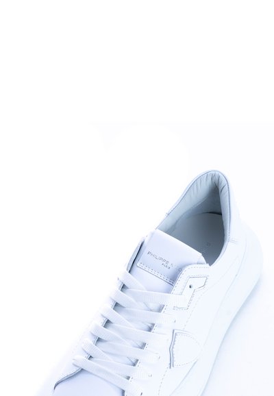 Baskets en cuir blanc avec bout arrondi, lacets plats, col rembourré et logo subtile sur la languette. Texture lisse et design minimaliste.