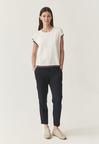 Top bianco a maniche corte con bordi neri, abbinato a pantaloni blu scuro. I pantaloni presentano tasche e gamba affusolata, indossati con sneakers chiare.